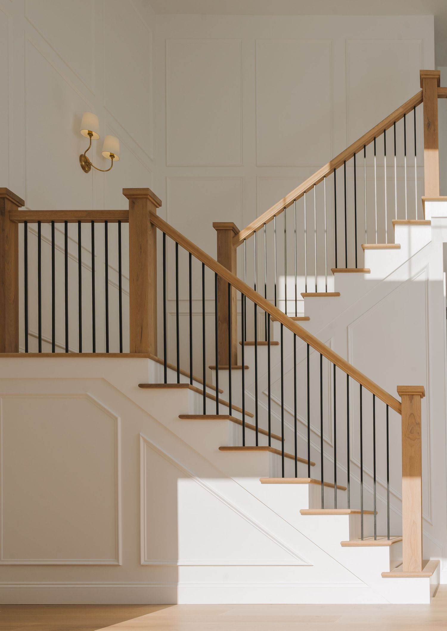 Elegant staircase with white paneling, wooden handrails, and black metal balusters in natural light.