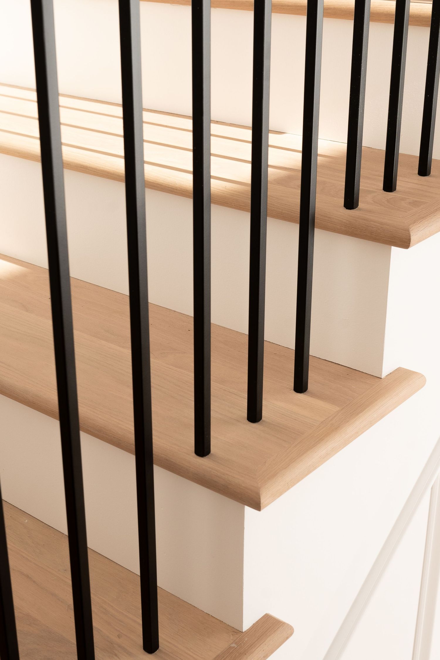 Close-up of black metal balusters against white risers and natural wood treads on a residential staircase.