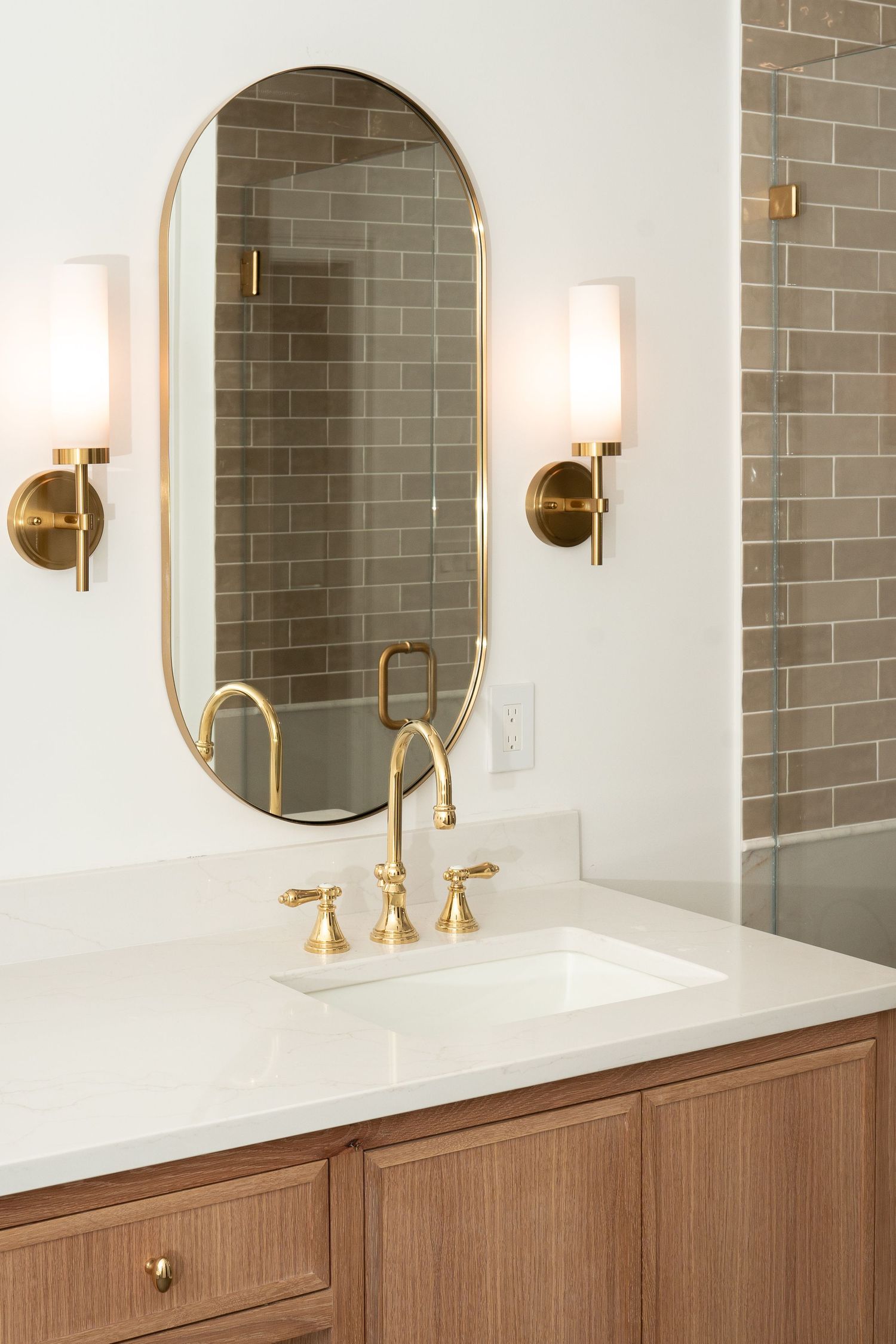 Luxury bathroom vanity with gray tile backsplash, brass sconces, and round mirror details.