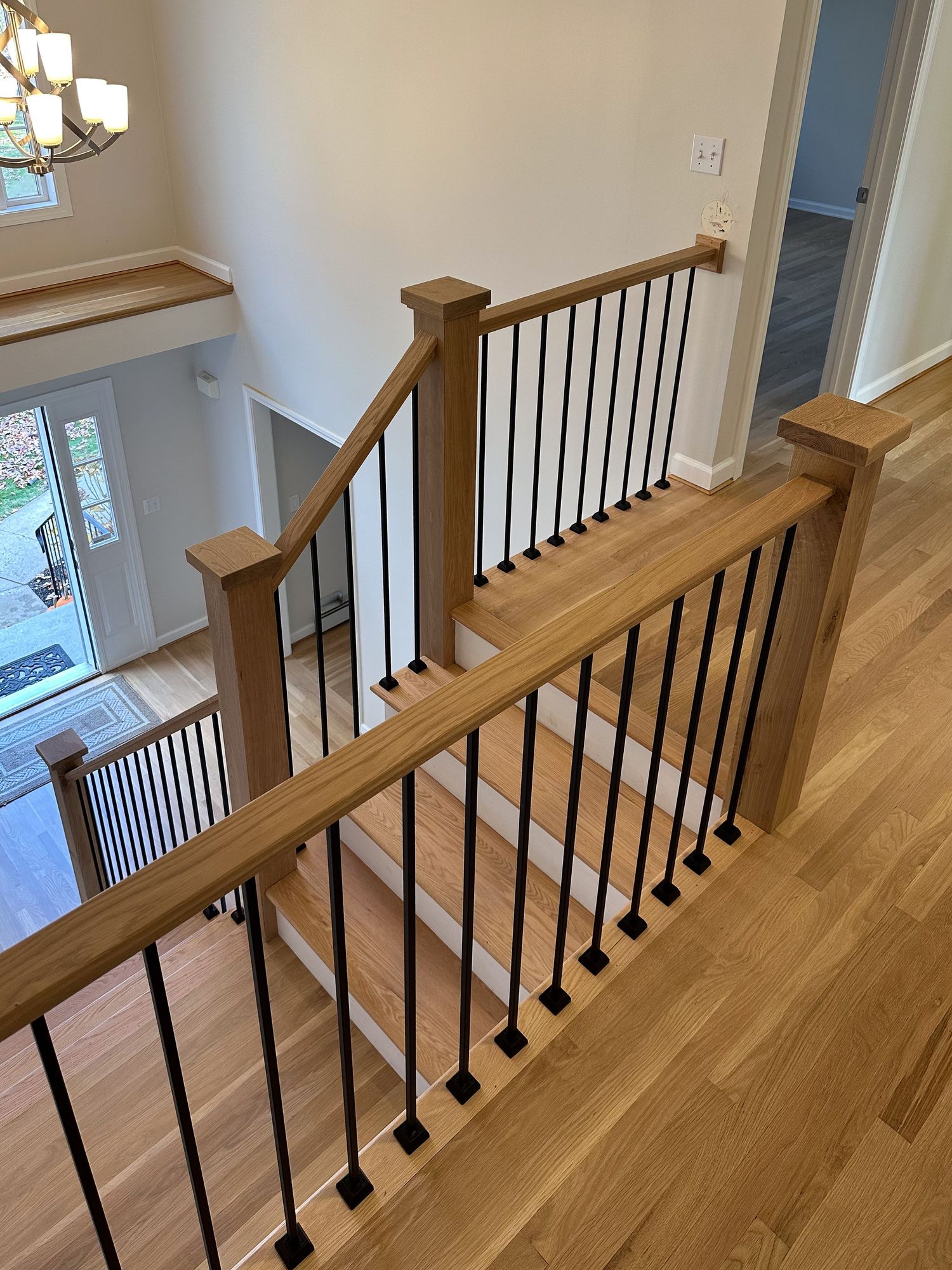 Modern staircase railing with wooden handrail and black metal spindles overlooking foyer.