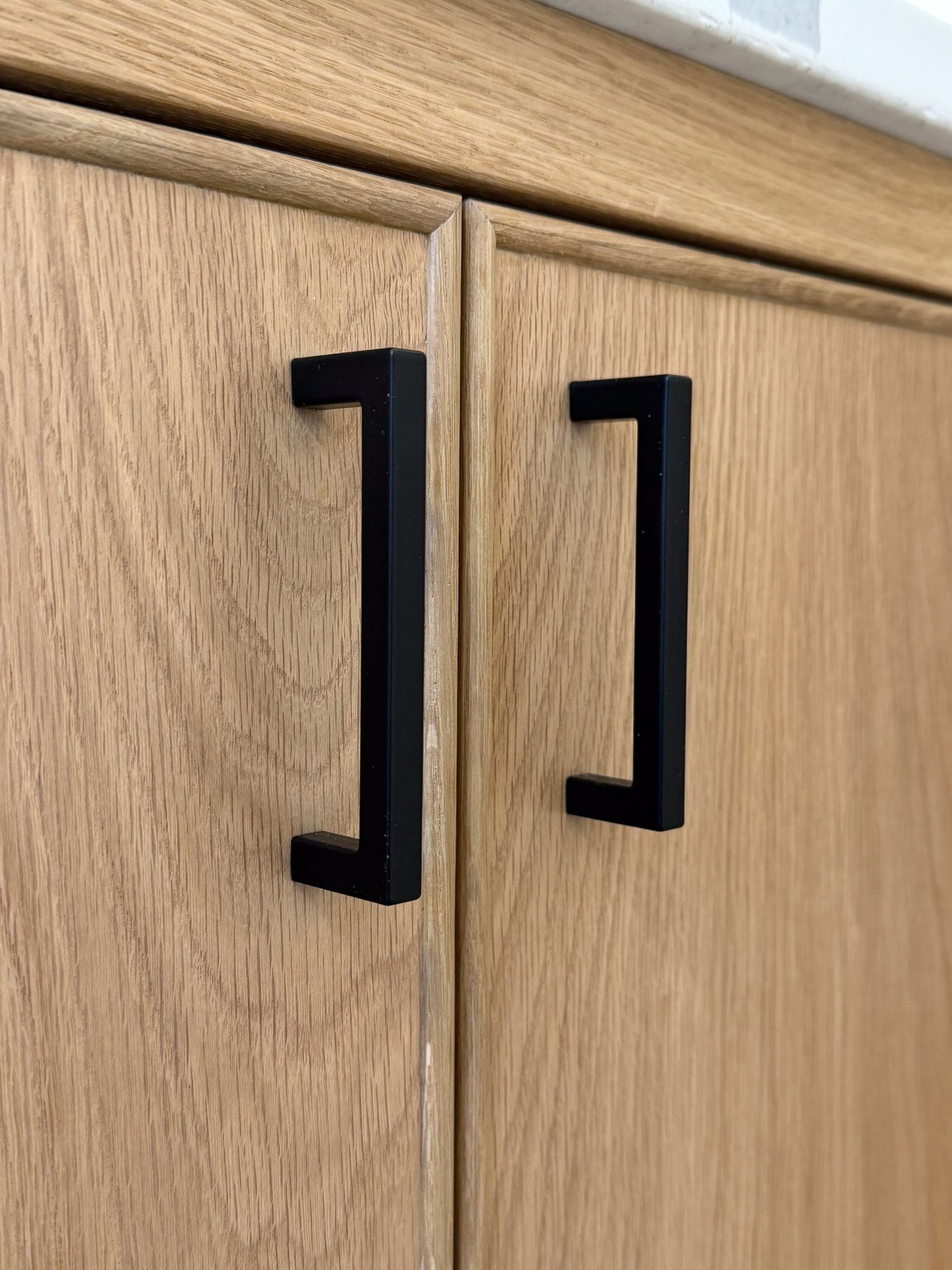 Black modern drawer pulls mounted on light wood cabinet doors showing minimalist design.