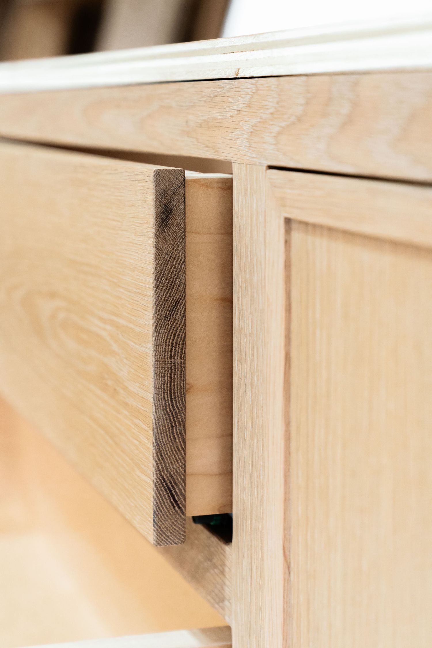 Close-up of a light oak wood drawer with a minimalist metal handle on a modern wooden cabinet.
