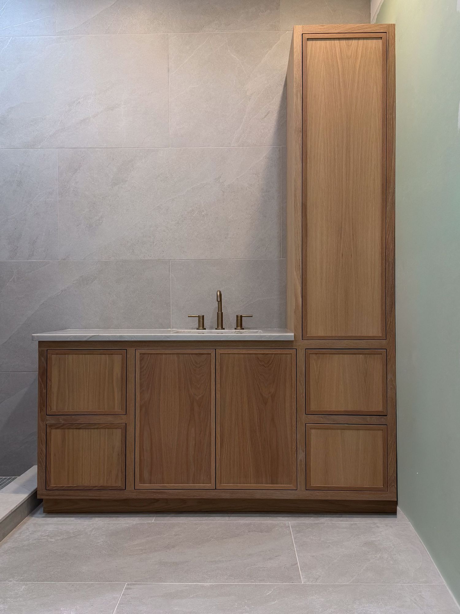 Modern bathroom cabinetry featuring light wood finish and tall storage unit against grey wall.