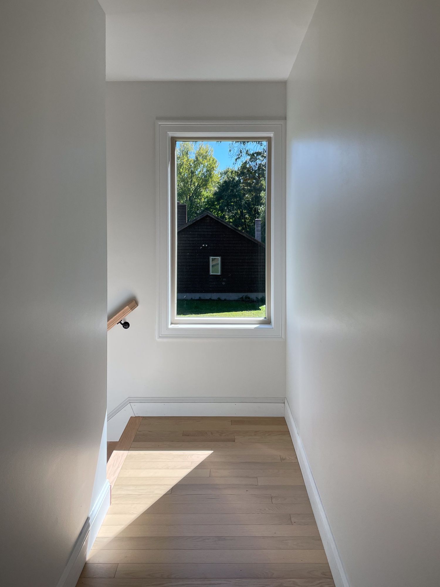 Bright hallway with hardwood flooring and large window letting in natural sunlight.