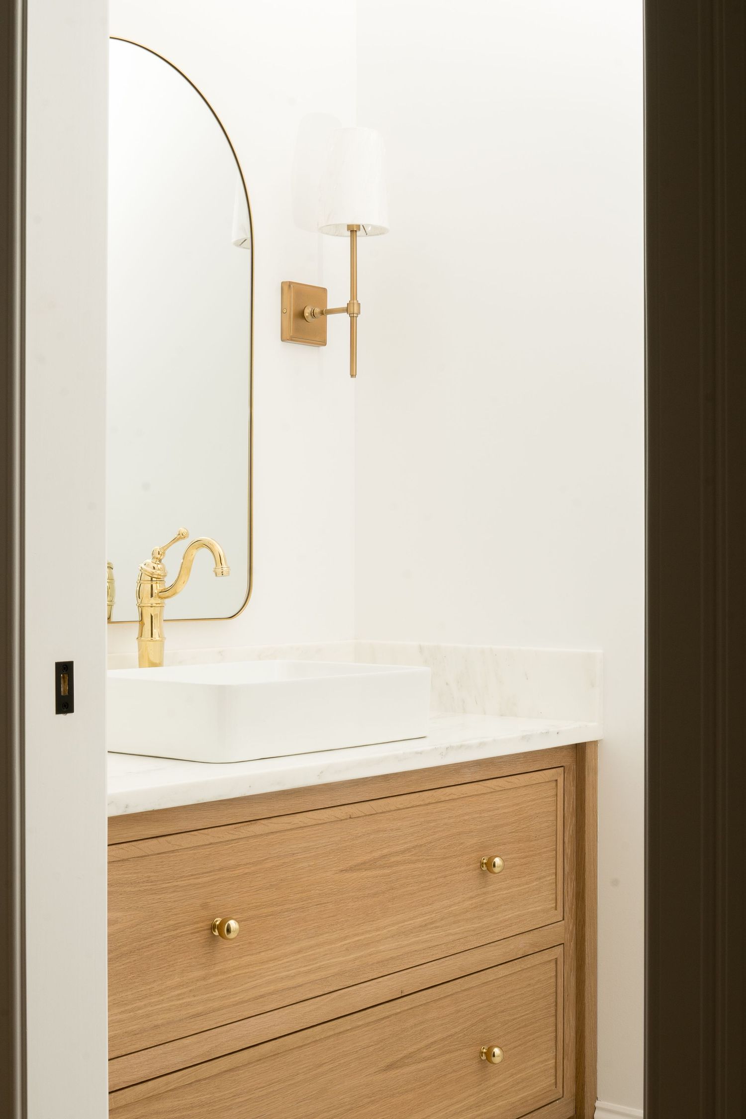 Modern bathroom vanity with brass fixtures and curved mirror against white walls.