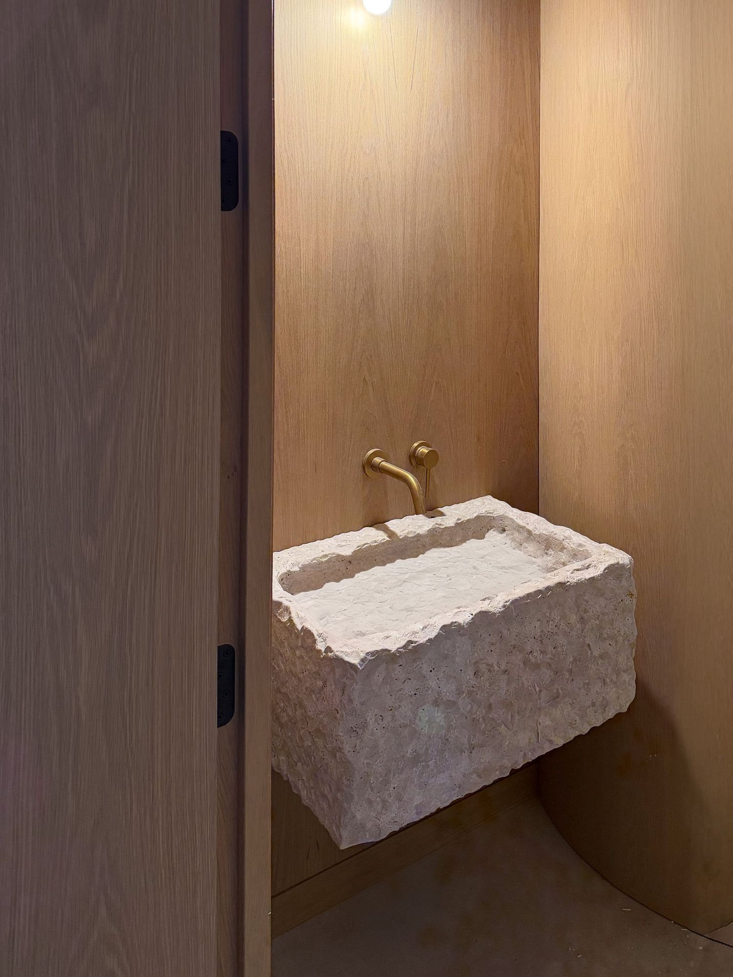 Modern powder room featuring a floating rough-cut stone sink basin with brass fixtures.