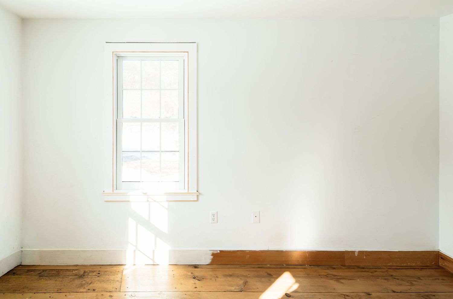 Bright empty room with white walls, wood floors and window letting in natural light.