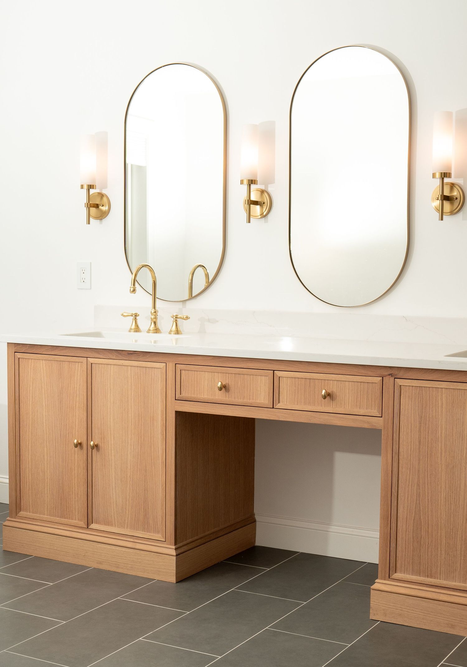 Double vanity with oval mirrors, brass fixtures, and light wood cabinetry in modern bathroom design.