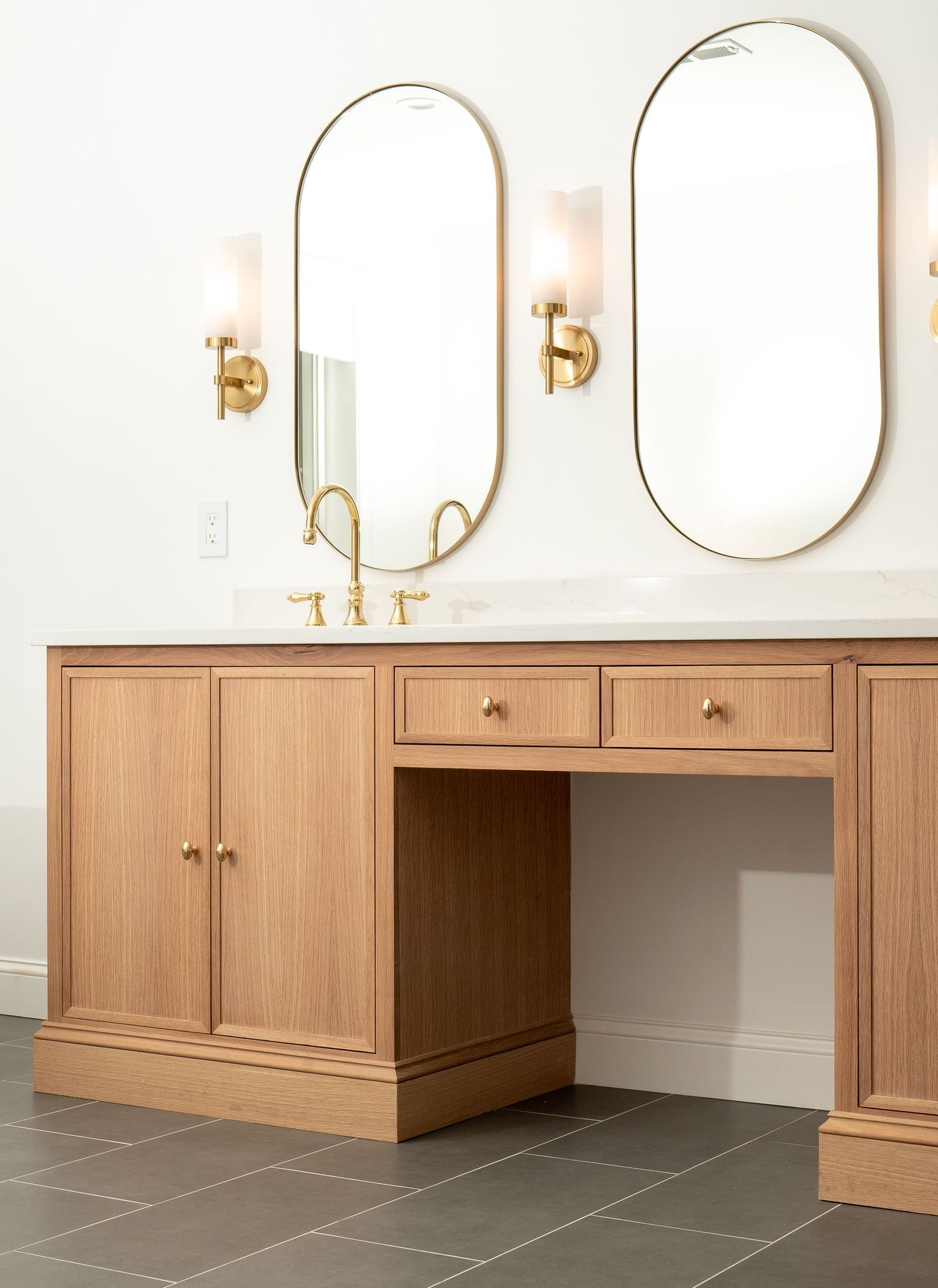 Modern bathroom vanity with light wood cabinets and oval mirrors mounted on white walls.