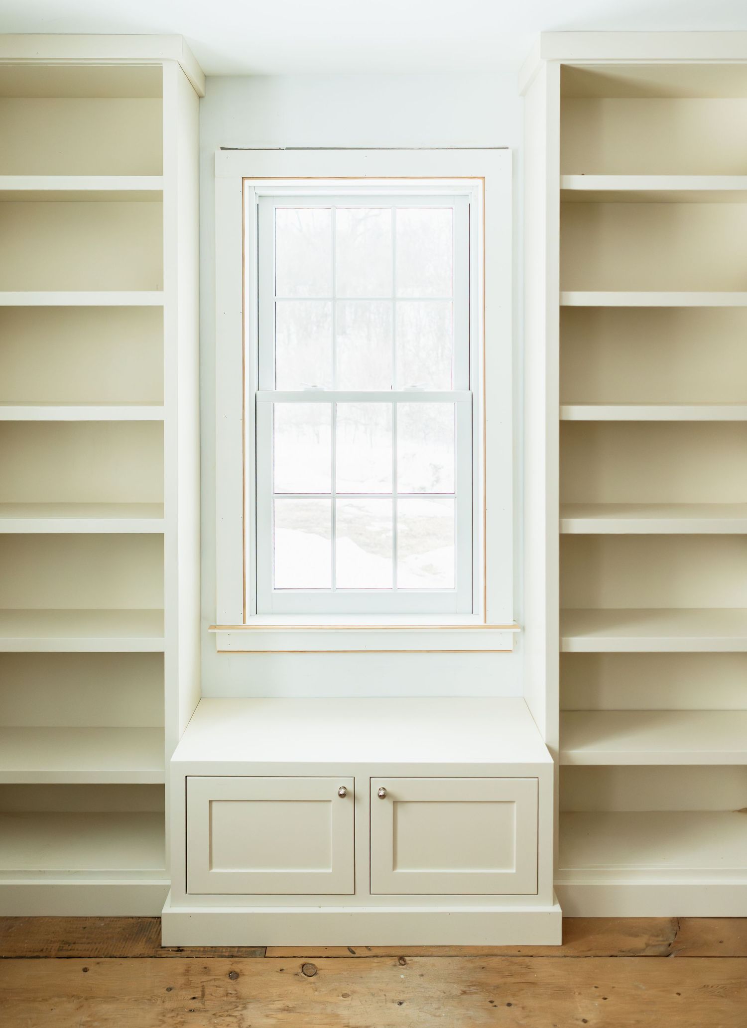 White built-in bookshelves surrounding a window create a classic library-style wall unit.