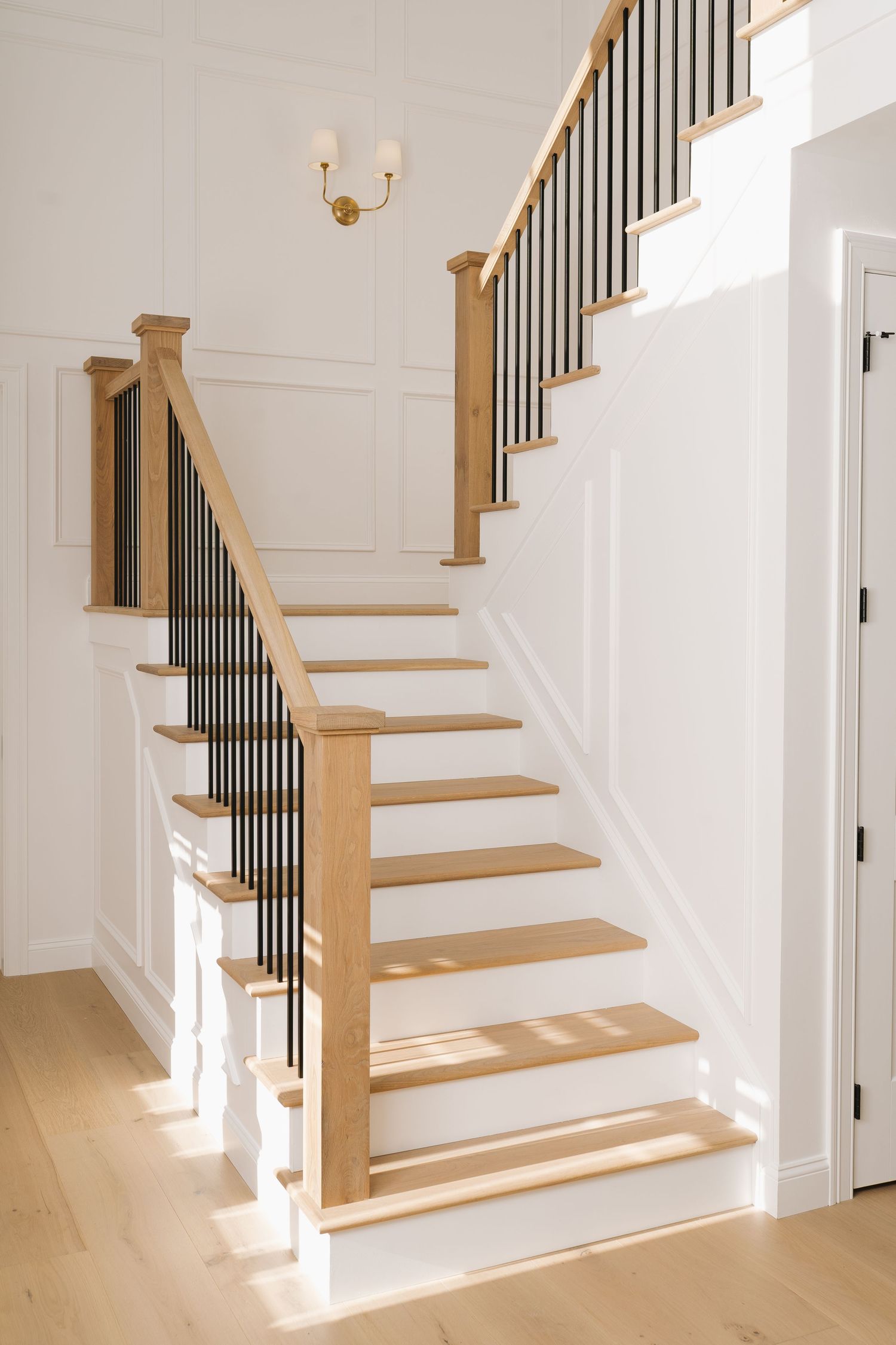 Modern staircase with light wood treads, white risers, and black metal balusters creates an elegant transitional design.