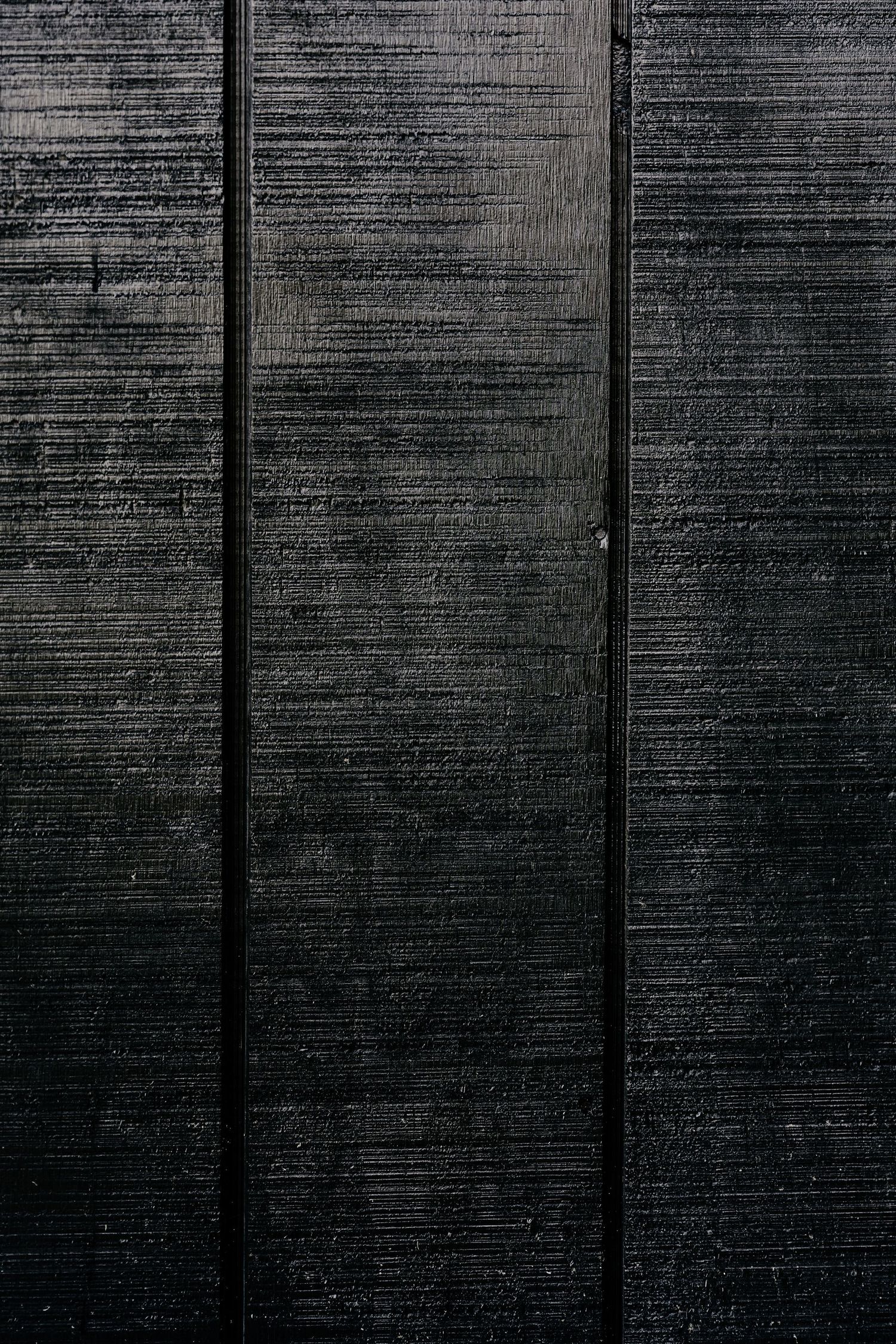 Dark charred black wood vertical planks with a rough brushed texture and narrow gaps between each board.