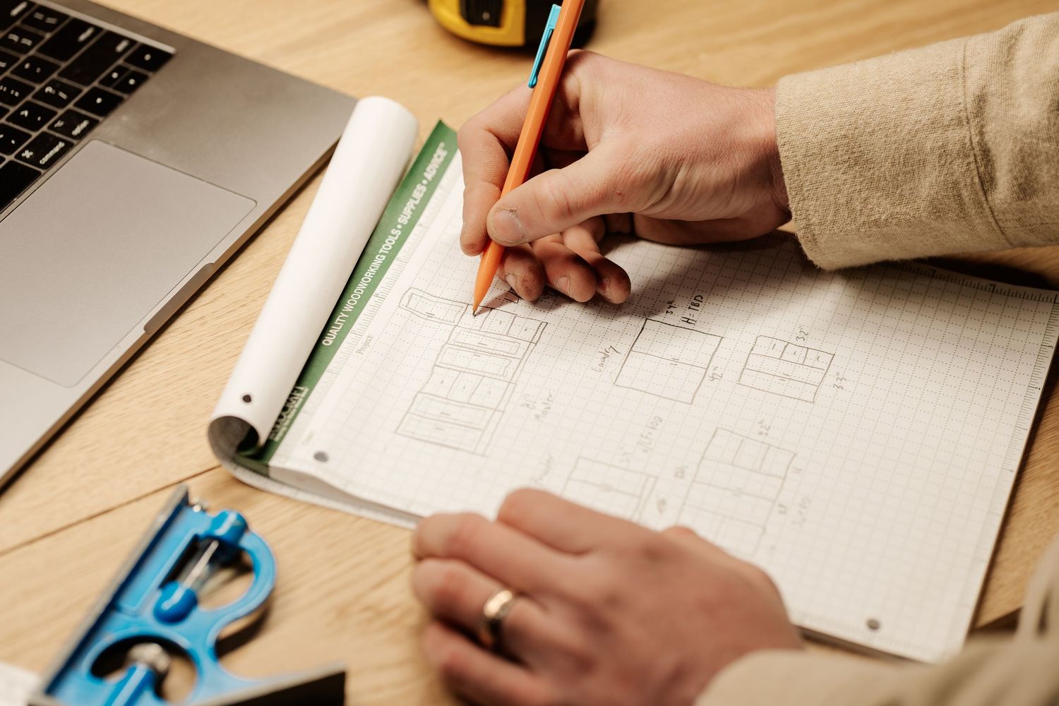 Hands working on architectural drawings and blueprints with measuring tools on wooden desk.