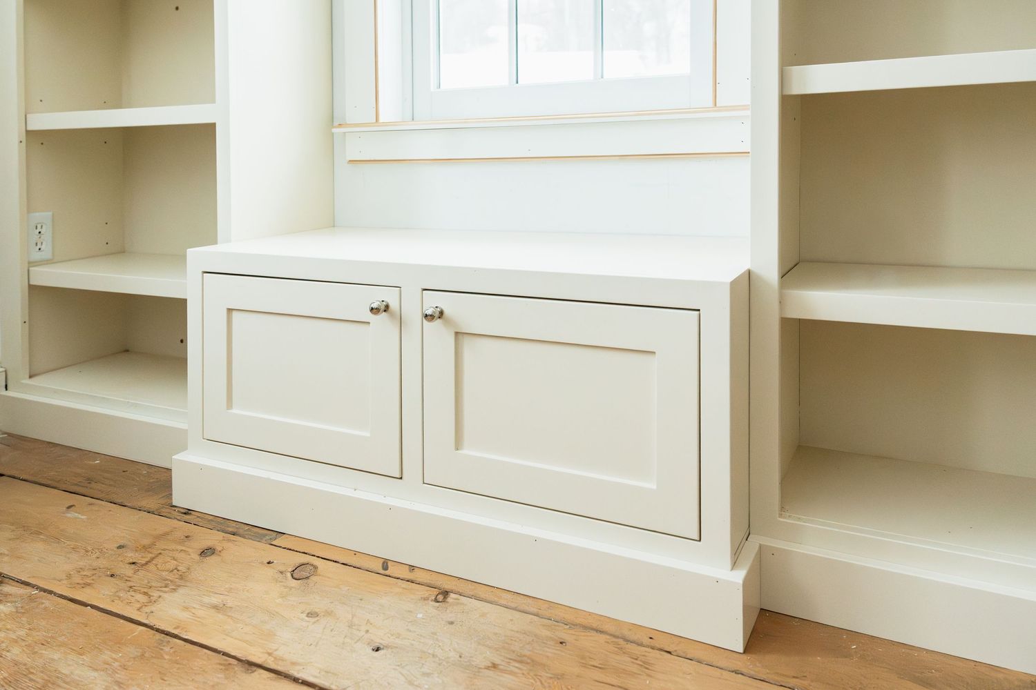White built-in shelving and cabinets with window seat creating a cozy reading nook.