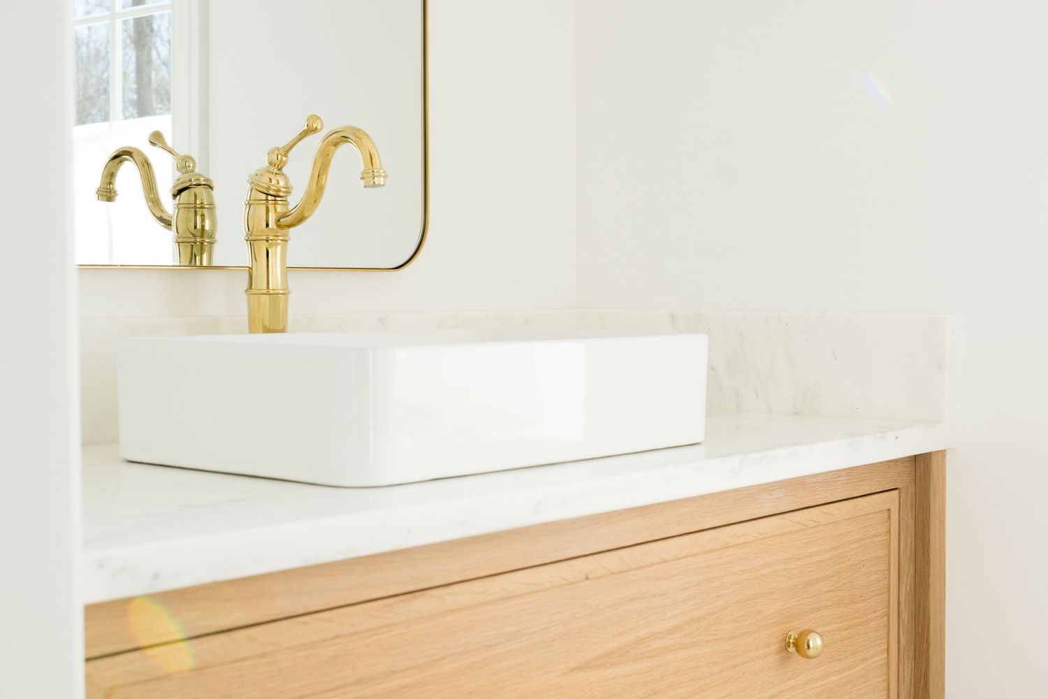 Contemporary bathroom with light wood vanity, white countertop, and brass hardware details.