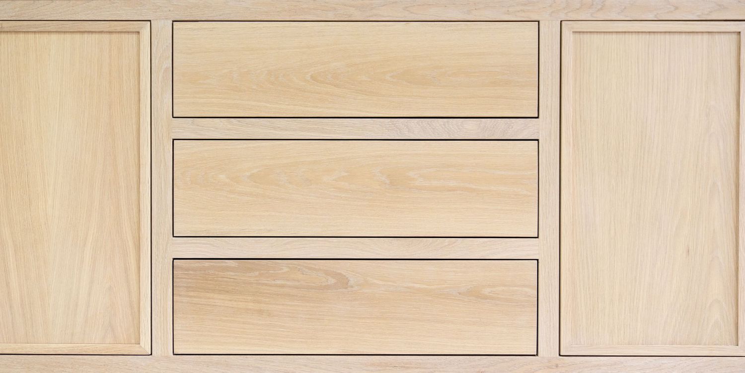 Light oak wood cabinet with three center drawers flanked by two panel doors, showcasing natural wood grain texture.