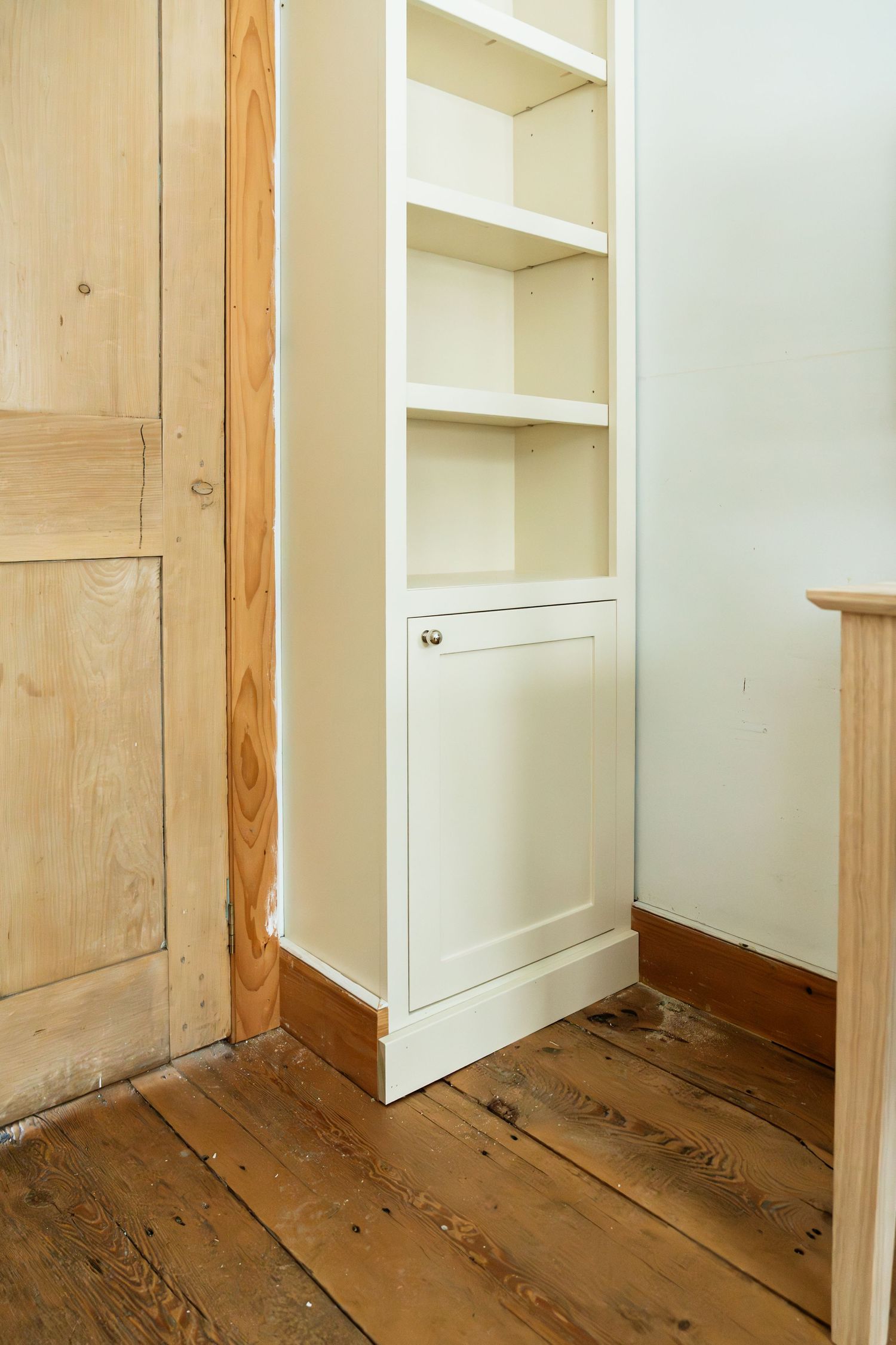 White built-in shelving unit with cabinet door and wood trim details.
