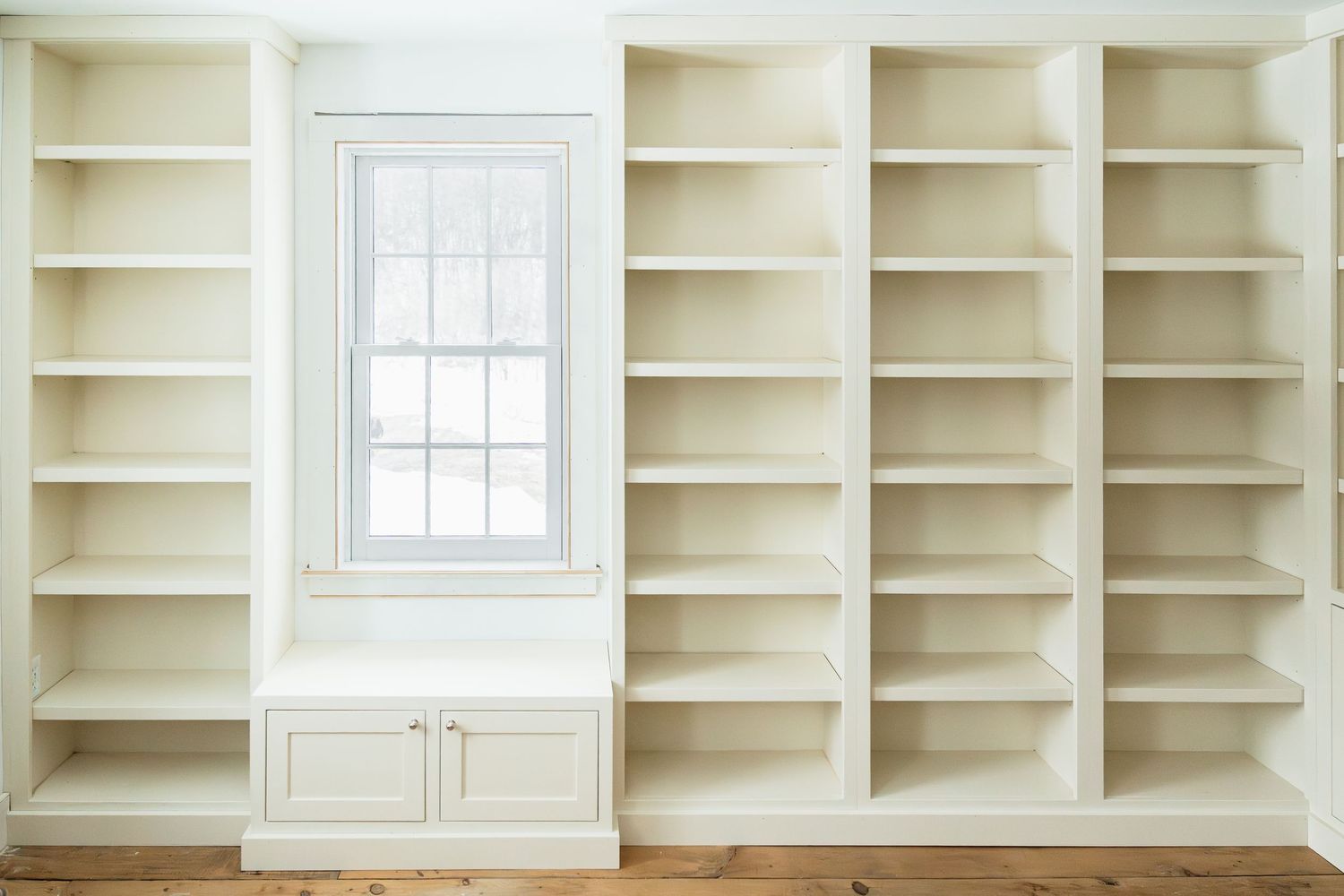 Built-in white bookshelf wall unit with window and cabinet storage beneath.