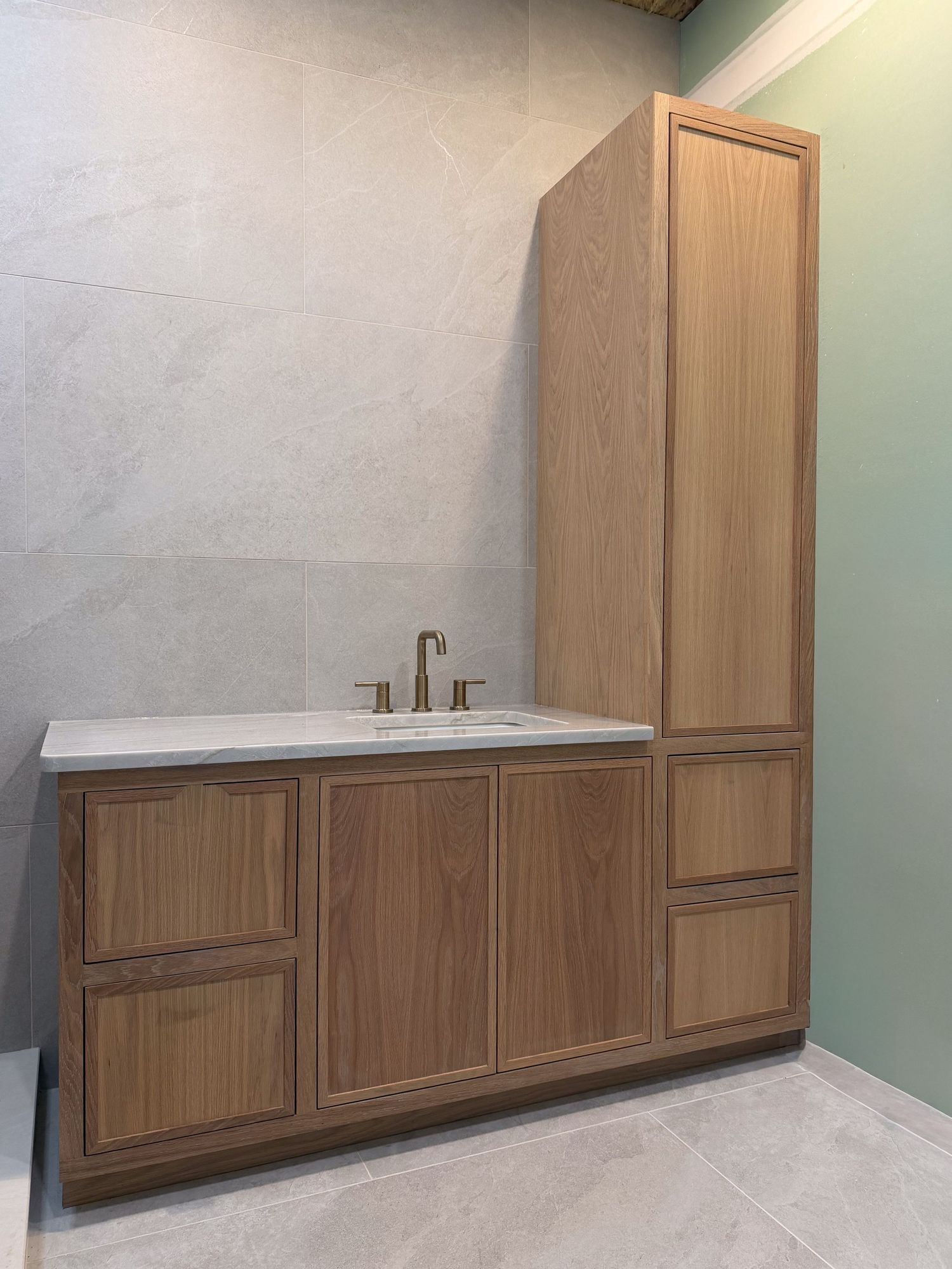 Custom bathroom vanity with tall cabinet and marble countertop against concrete-look wall.