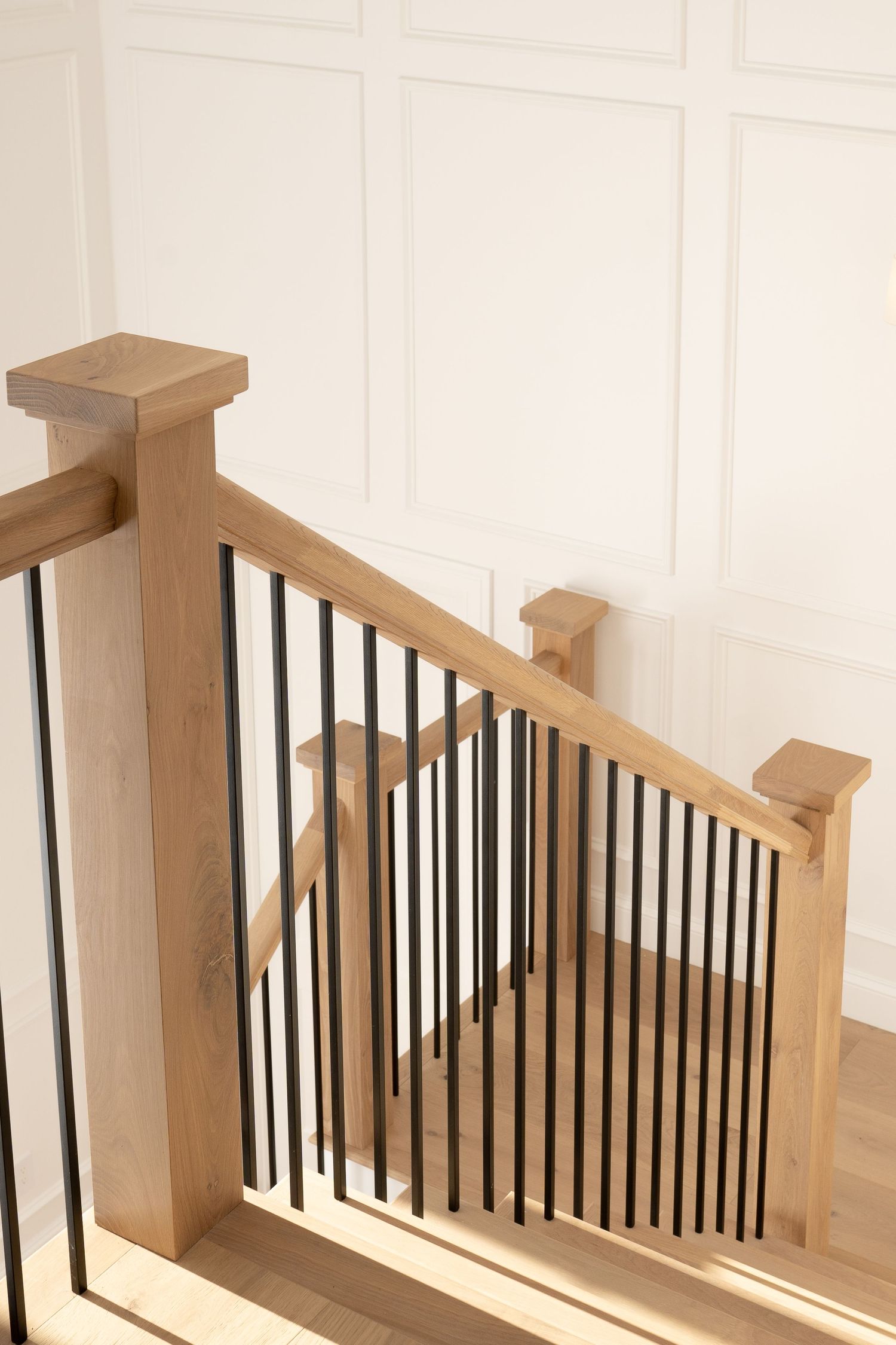 Close-up view of wooden handrail and black metal balusters on a contemporary staircase design.