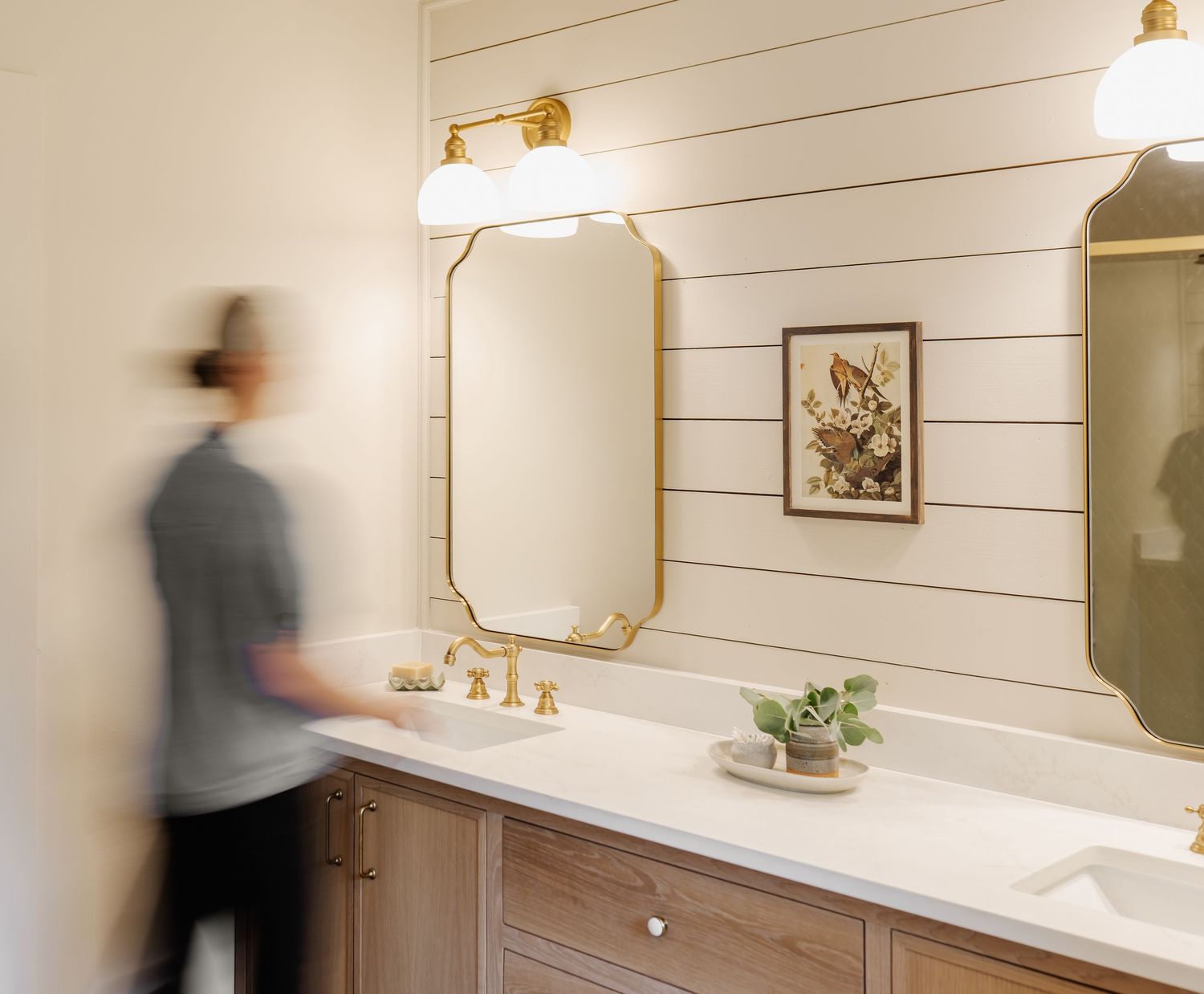Modern bathroom with gold fixtures, shiplap walls, dual vanity, and octagonal mirrors illuminated by warm sconce lighting.