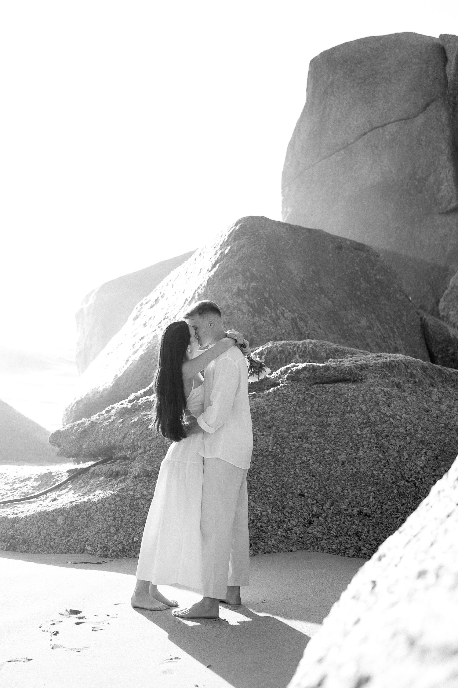 Black & white photo of the couple kissing during golden hour at Camps Bay, Cape Town.