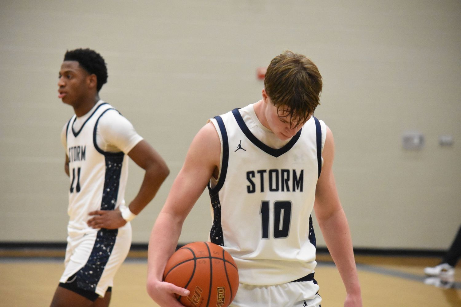 Two Storm basketball players in white jerseys stand on court during game.