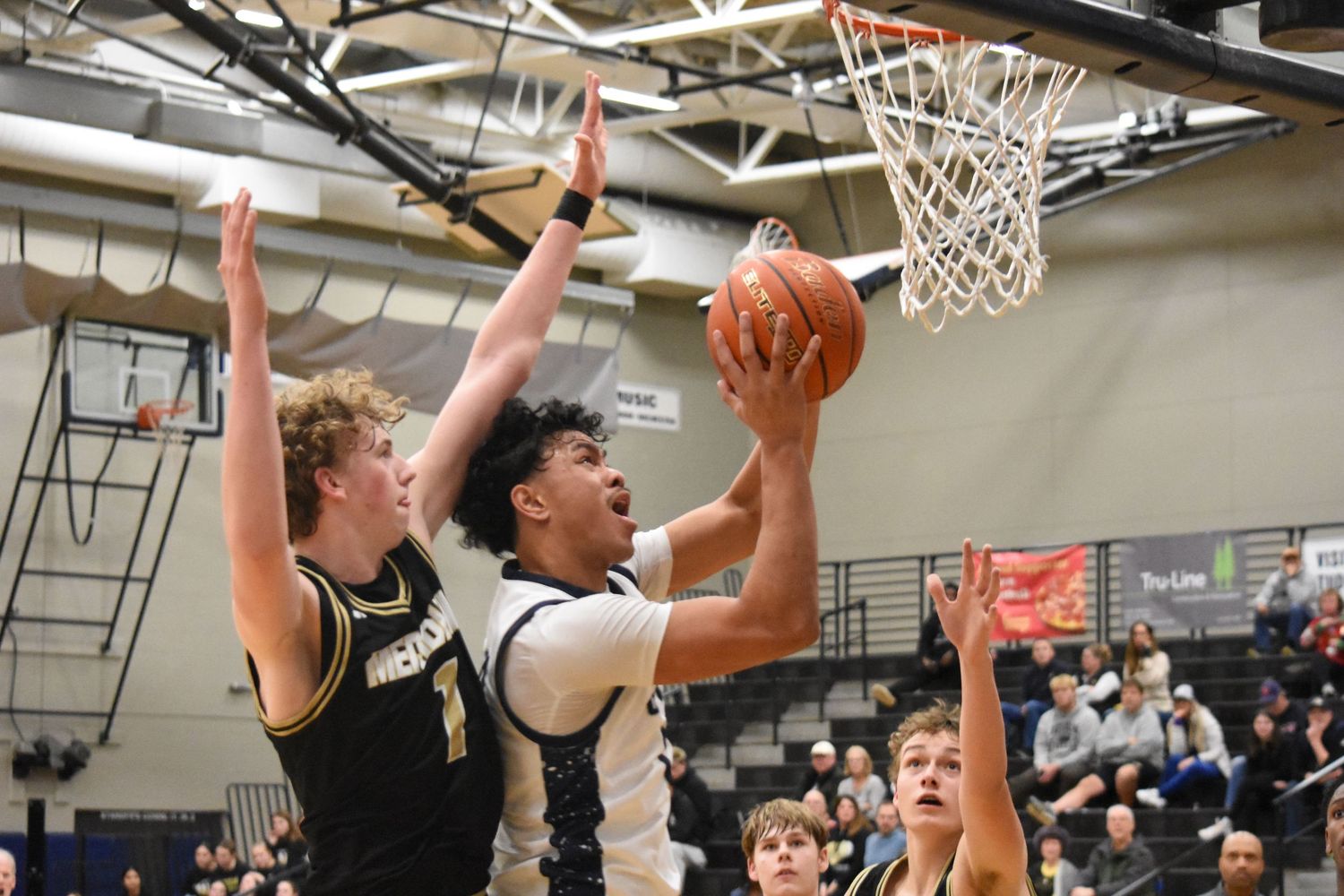 Players compete for shot under basket during intense basketball game action.