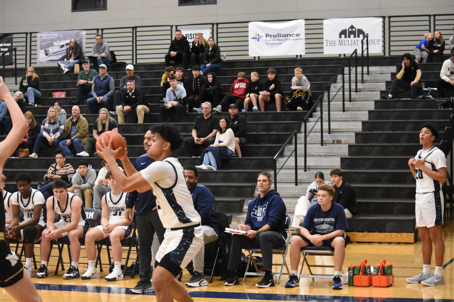 Basketball player prepares to shoot during game with spectators in bleachers behind.