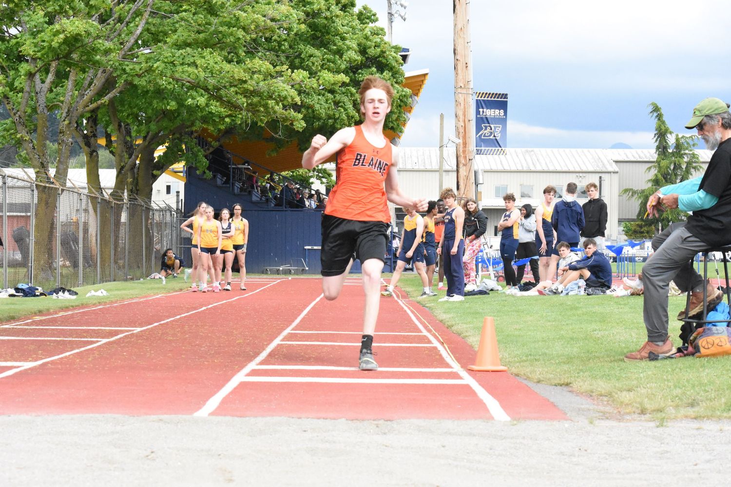 Athletes competing in long jump events at an outdoor track and field competition with spectators watching from sidelines.