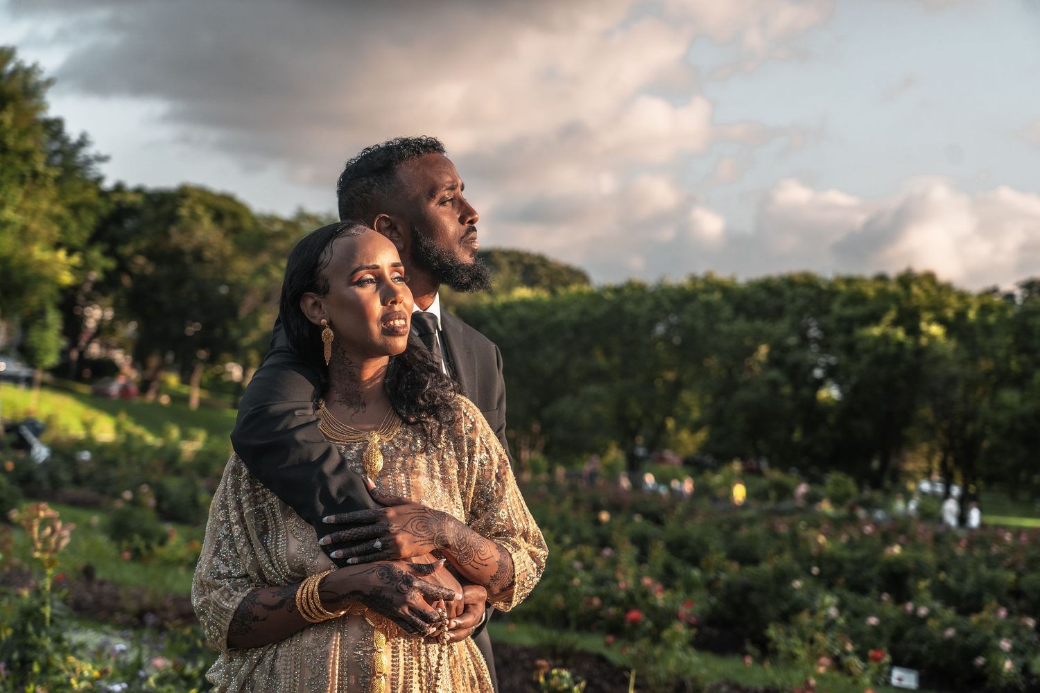 Couple embracing in a lush rose garden at golden hour in elegant traditional attire.