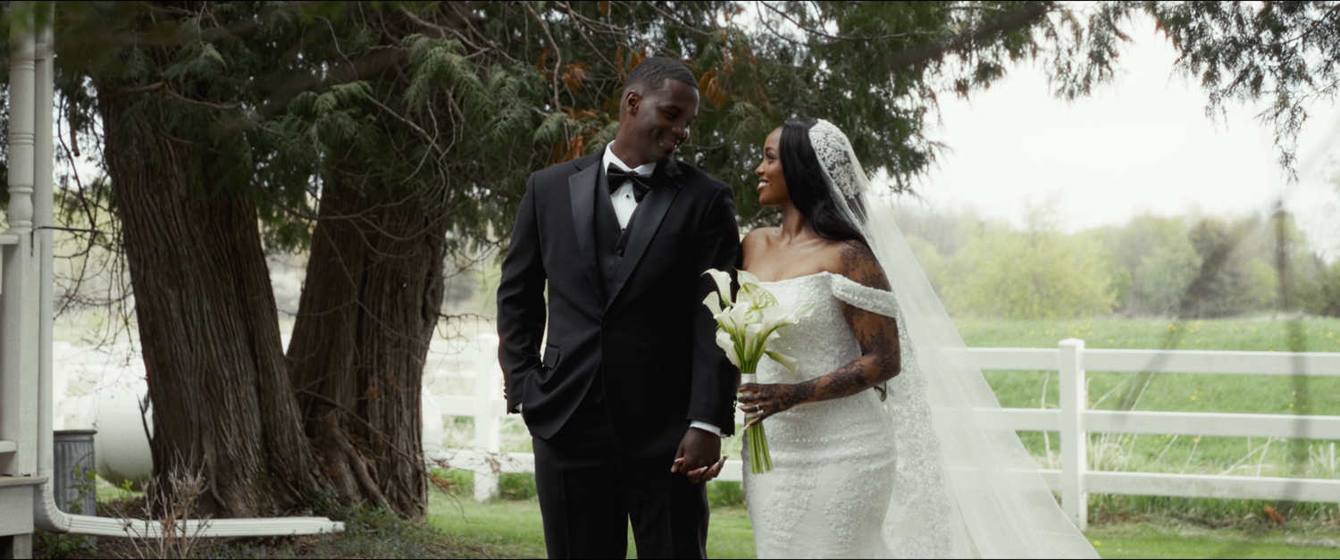 A bride and groom share a romantic moment outdoors near a large tree, with the bride in a white gown and groom in a black tuxedo.