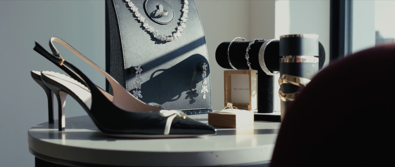 Elegant black slingback heels displayed on a white table beside a camera lens and accessories in a stylish setting.