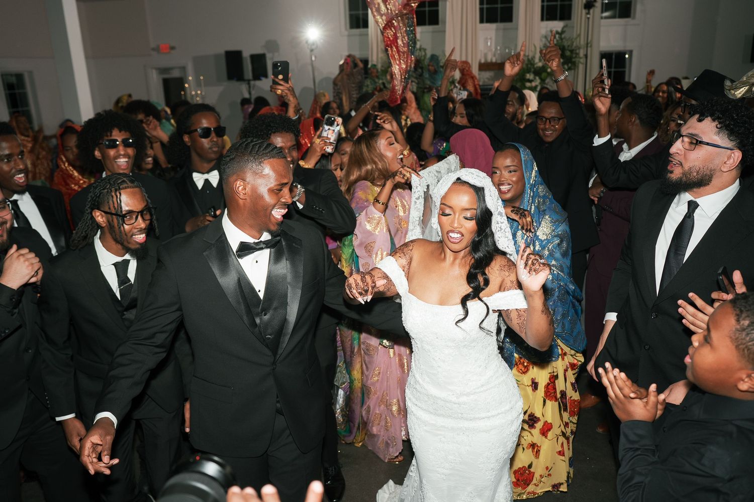 Joyful bride and groom dancing with guests at a lively wedding reception celebration.