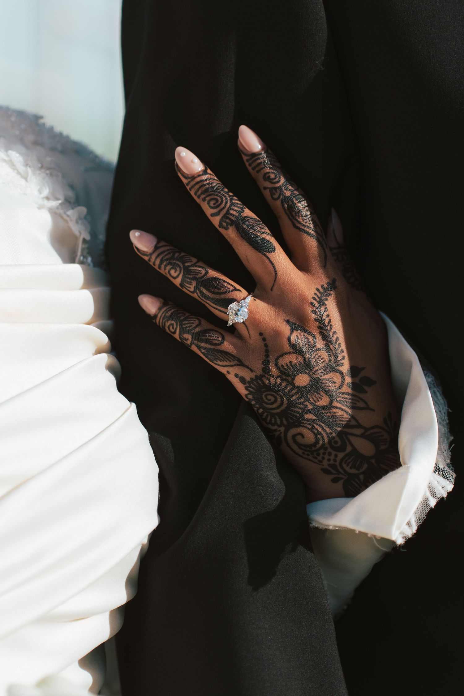 Close-up of bride's henna-decorated hand with diamond engagement ring against groom's dark suit.