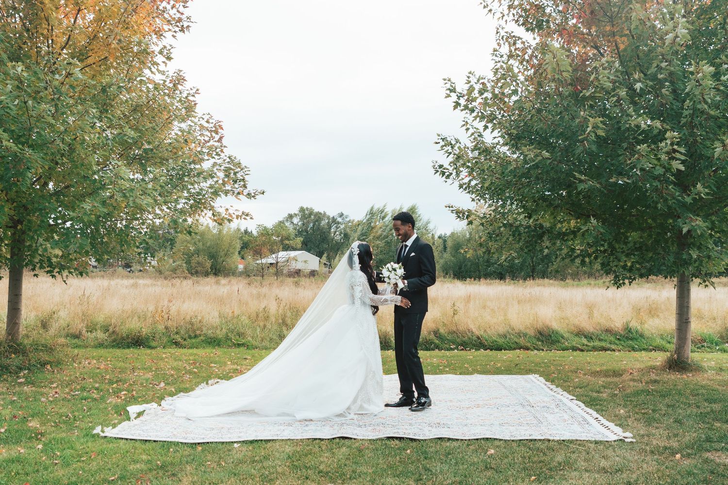 Bride and groom standing on a blanket surrounded by autumn trees in an outdoor wedding ceremony.