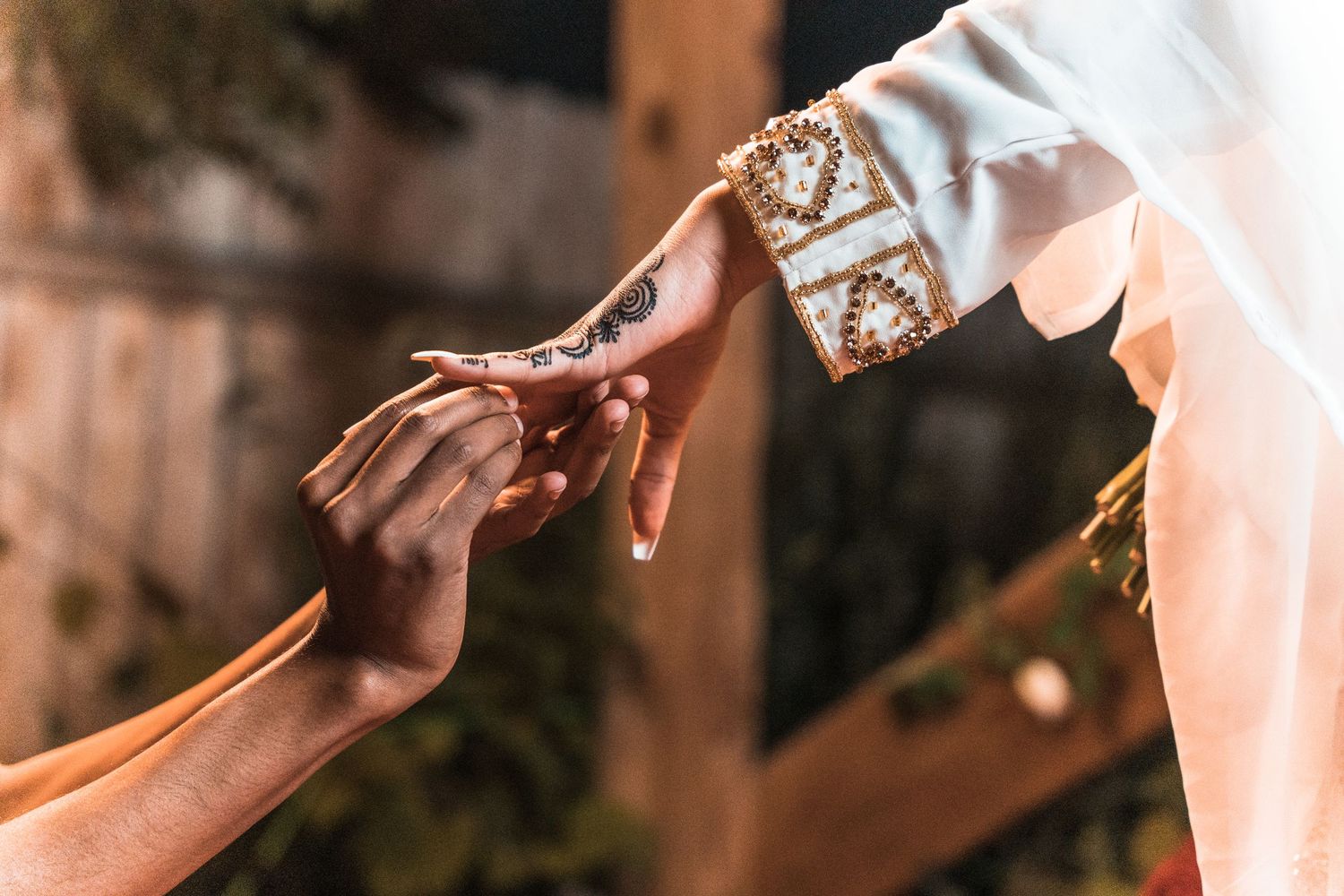 Close-up of bride with henna-adorned hand receiving ring during traditional South Asian wedding ceremony.