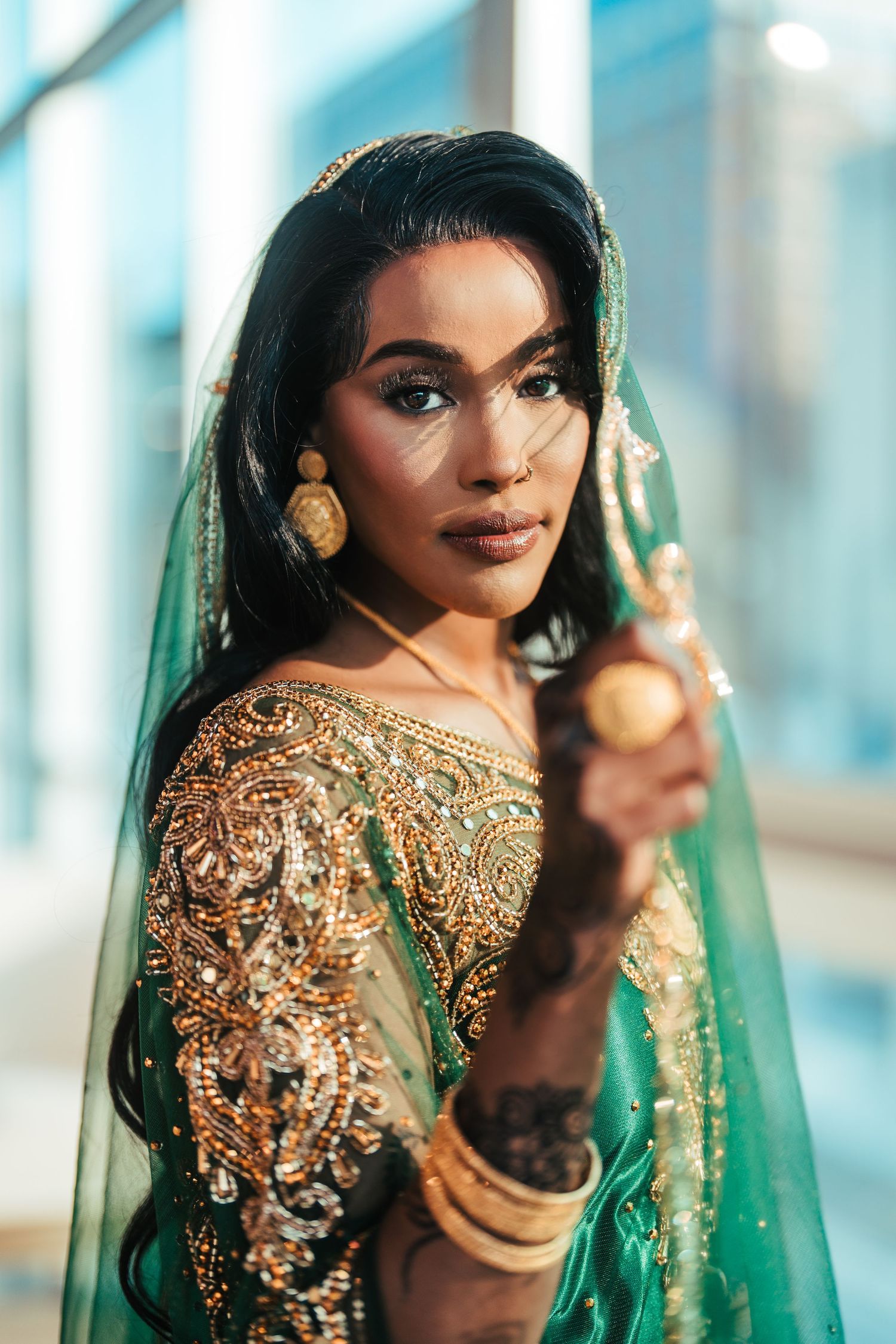 Beautiful woman in green and gold Indian bridal lehenga with henna, gold bangles, and dupatta holding gold accessory.