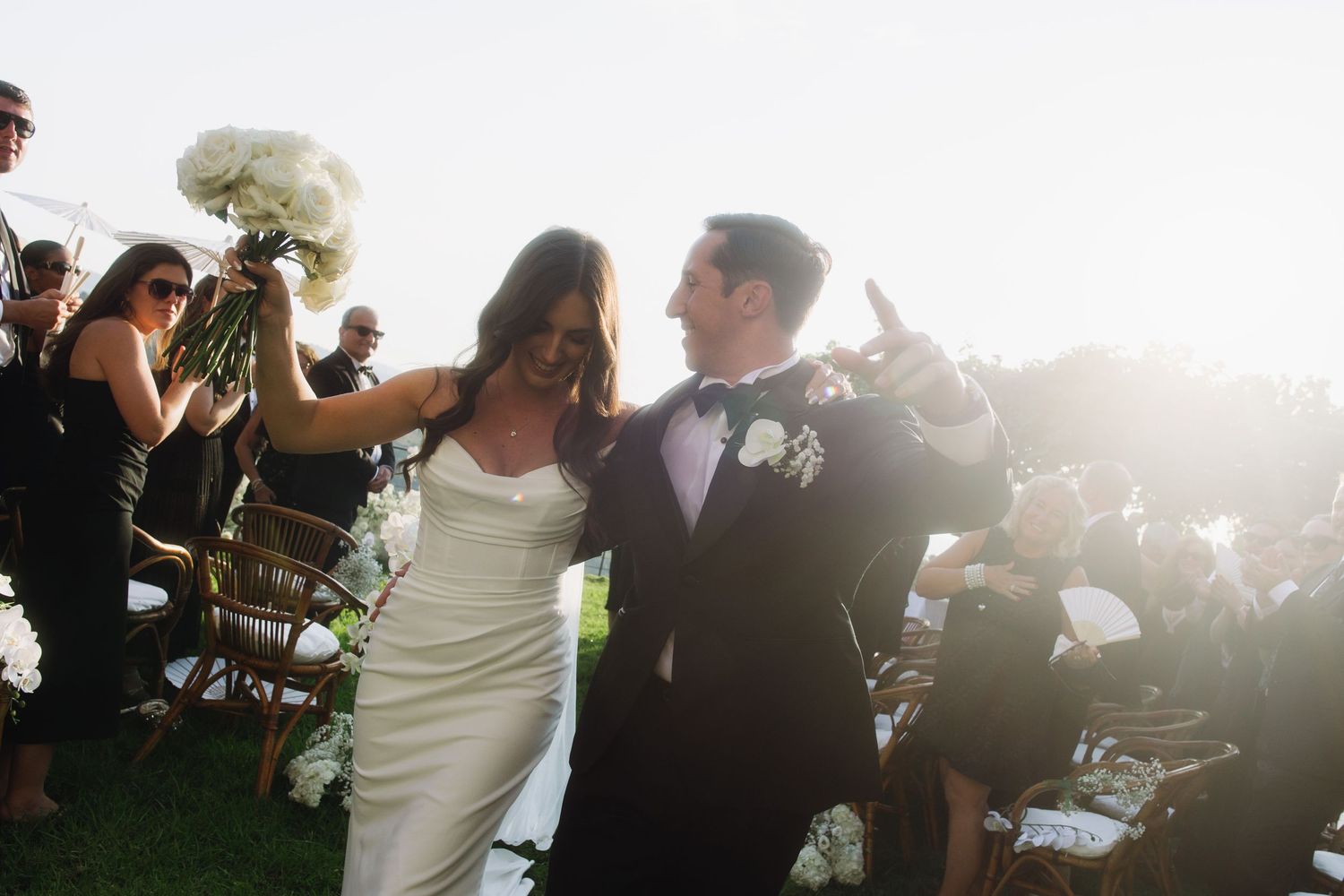 Wedding guests dance and celebrate on a sunlit outdoor dance floor during a joyful reception celebration.