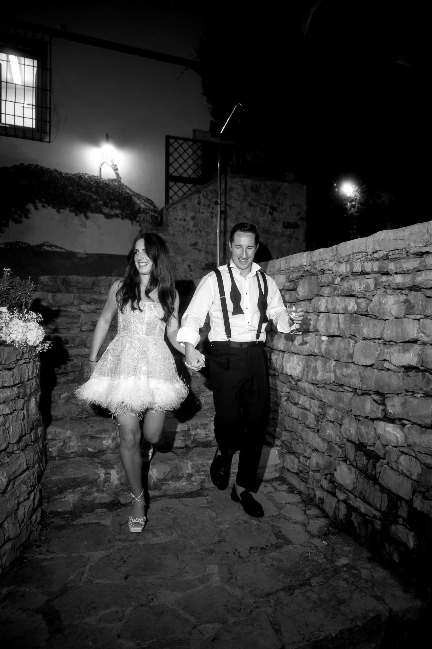 Black and white photo series of a couple in formal attire sitting on a stone wall at night.