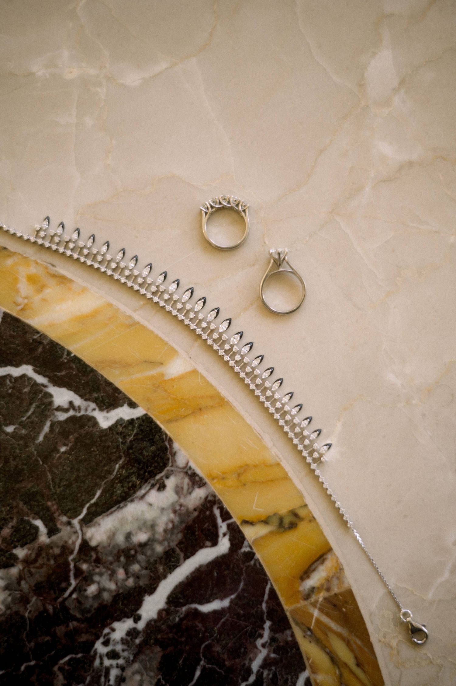 Wedding rings rest on a marble surface with an elegant curved architectural detail featuring gold and black marble accents.
