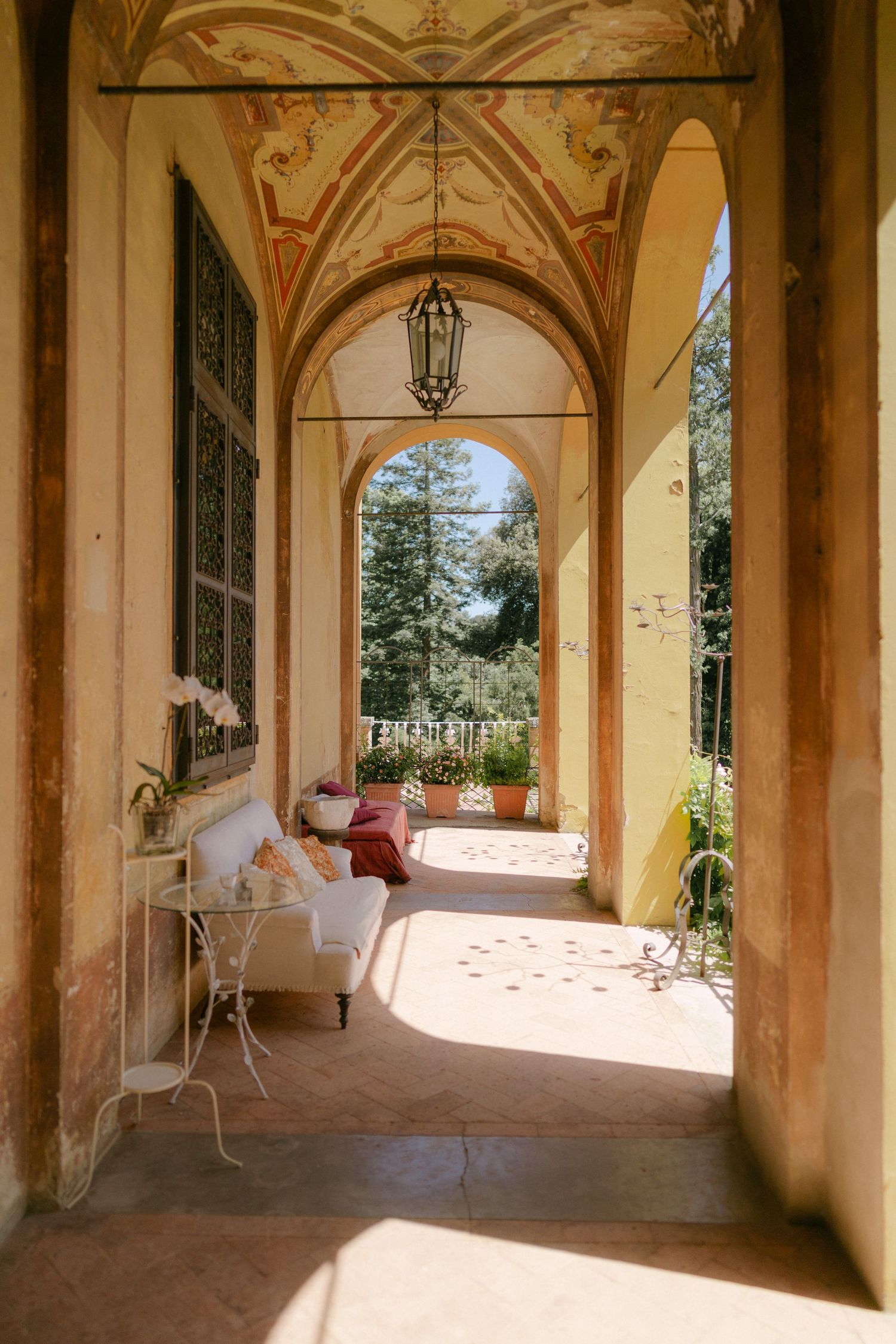 Sunlit arched colonnade walkway in a Mediterranean villa with terracotta floors and garden views through the columns.
