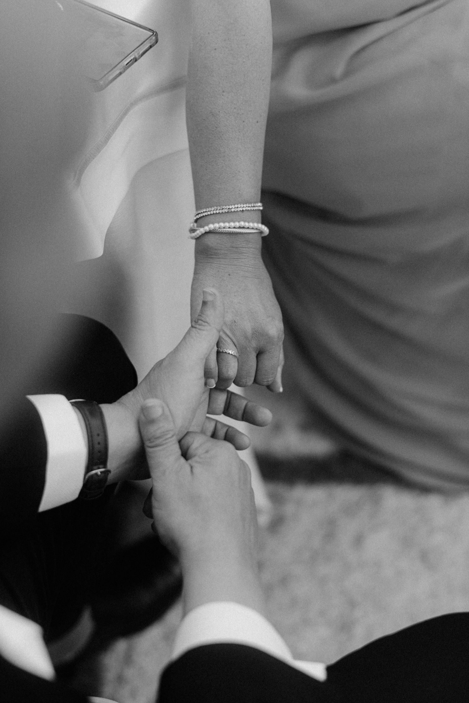 Black and white closeup of hands during a wedding ring exchange ceremony, with a pearl bracelet visible.