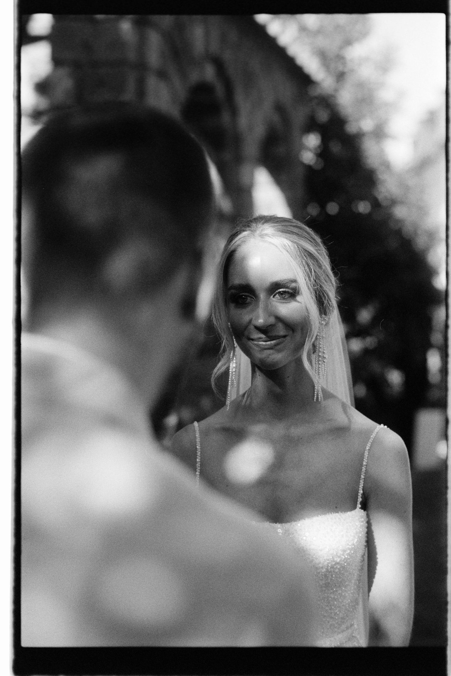 Black and white wedding photo of a bride smiling warmly while looking at her partner on their special day.