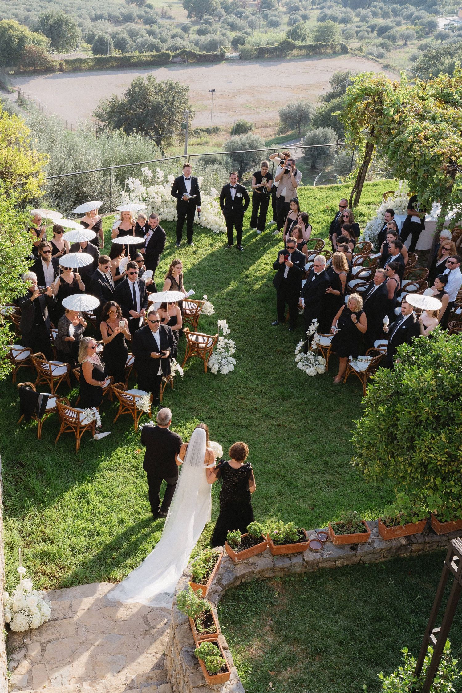 An outdoor wedding ceremony on a grassy hillside with guests seated in rows overlooking a scenic valley view.