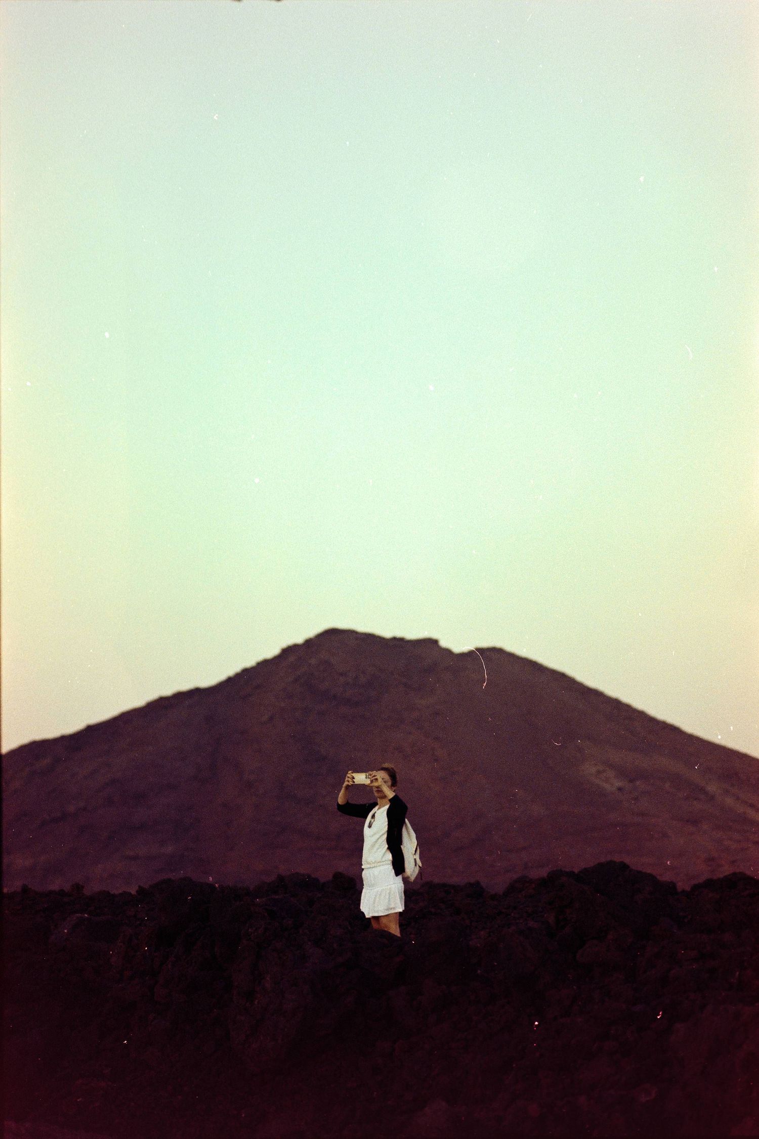A silhouetted figure stands against a mountain landscape at dusk with a soft gradient sky in the background.
