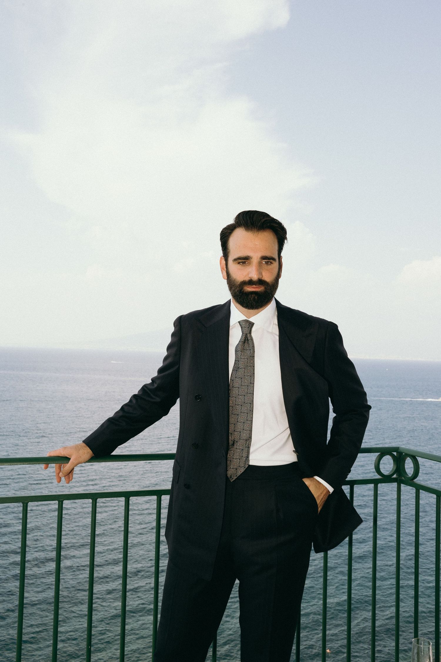 A bearded man in a business suit stands at an oceanside railing in a series of similar poses.