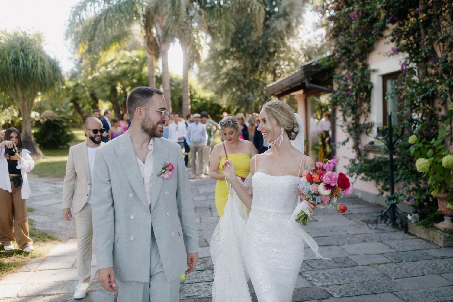 A joyful wedding celebration at a scenic venue with palm trees and garden surroundings on a sunny afternoon.
