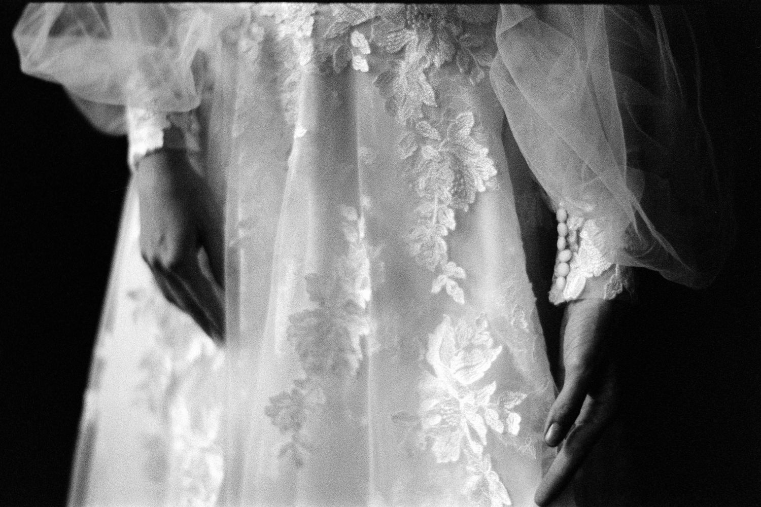 Close-up black and white photo of a delicate lace wedding dress with floral embroidery details.