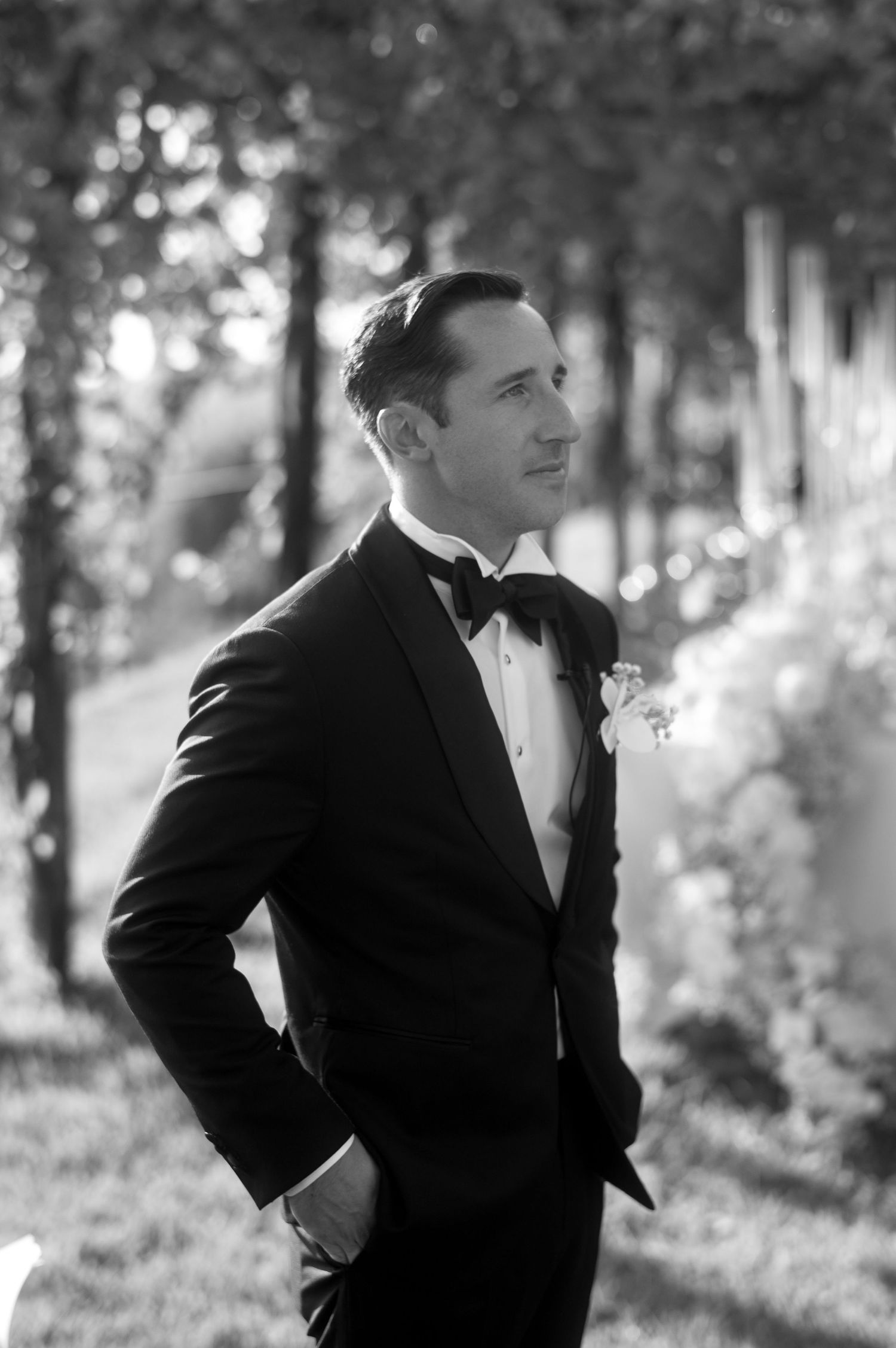 Black and white candid photograph showing a couple in formal attire laughing together in a sunlit outdoor setting.